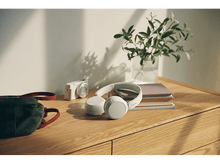 Charger l'image dans la galerie, Un bureau en bois avec un casque, un appareil photo, un journal et une plante dans un vase en verre. Soleil.