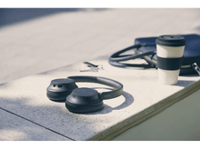 Charger l'image dans la galerie, Casque noir sur une surface, à côté d'une tasse et d'un sac. Le fond est une journée ensoleillée.