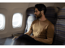 Charger l'image dans la galerie, Un homme portant des écouteurs est assis près d'une fenêtre dans un avion, regardant dehors.