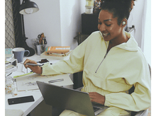 Charger l'image dans la galerie, Une femme avec des écouteurs, dessinant sur papier sur un bureau avec un ordinateur portable et un téléphone.