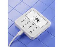 Charger l'image dans la galerie, Terminal de paiement blanc sur des carreaux bleus. Affiche un symbole de paiement sans contact.