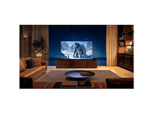 Charger l'image dans la galerie, Salon avec grand téléviseur montrant une scène de montagne enneigée. Canapé en cuir, meubles bruns.