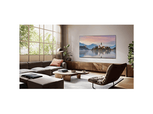 Charger l'image dans la galerie, Un salon avec une grande télévision affichant un paysage, un canapé marron et une table basse en bois.