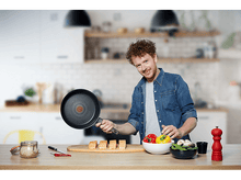 Charger l'image dans la galerie, Un homme tenant une poêle, préparant de la nourriture sur une planche de bois avec du saumon et des légumes.
