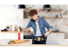 Charger l'image dans la galerie, Homme cuisinant du saumon dans une poêle noire sur une plaque de cuisson, planche en bois avec saumon, flou.