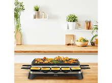 Charger l'image dans la galerie, Gril à raclette avec de la nourriture dessus. Fond de cuisine avec plantes et étagères.