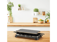 Charger l'image dans la galerie, Gril à raclette sur un comptoir en bois, avec des plantes et un fond en bois.