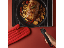 Charger l'image dans la galerie, Viande rôtie avec légumes dans une poêle, manique rouge et main tenant une poignée.