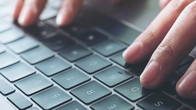 Un gros plan sur un clavier d'ordinateur. Des doigts tapent sur les touches.