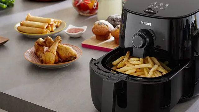Un airfryer posé sur un plan de travail sur lequel se trouve différents plats.