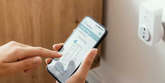 Gros plan sur un smartphone. On distingue en arrière plan une prise connectée.