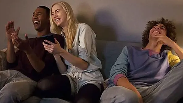Un groupe de jeune gens rient sur un canapé, l'un d'entre eux tient un téléphone dans sa main.