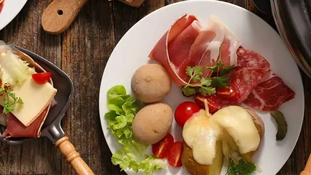 Une assiette de charcuterie, salade, pommes de terre et fromage fondu sur une table en bois.