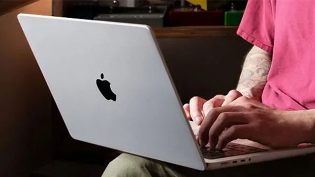 Une personne tape sur les touches du clavier de MacBook. L'ordinateur est posé sur ses genoux.