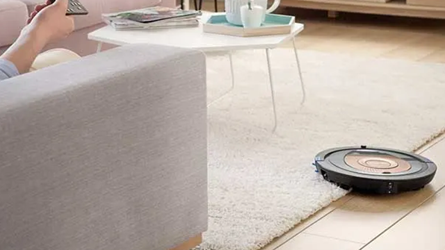Une personne assise sur son canapé se détend pendant qu'un robot aspirateur fait le ménage.
