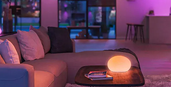 Une lampe connectée sur une table basse diffusant une lumière chaleureuse dans une pièce de vie.