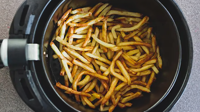 Vue du dessus de la cuve d'un airfryer remplis de frites dorées.