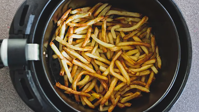 Un airfryer ouvert vue de dessus dans lequel se trouve des frites parfaitement cuites.