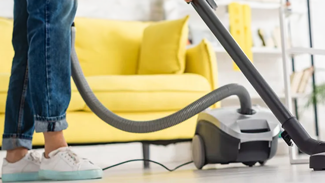 Une personne passe l'aspirateur devant un canapé jaune.