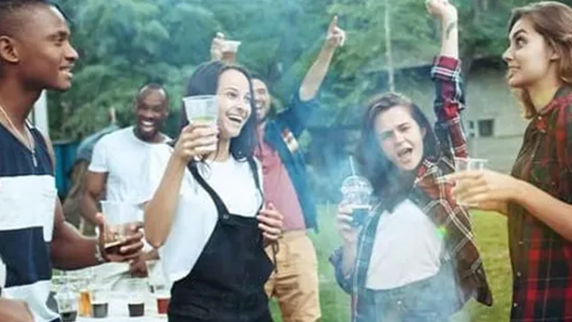 Un groupe de personne fait la fête avec des verres de la main. Ils sont en extérieur devant un barbecue duquel s'échappe de la fumée.