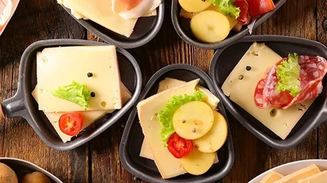 Vue de dessus de plusieurs poêlons à raclette contenant fromages, légumes et charcuteries.