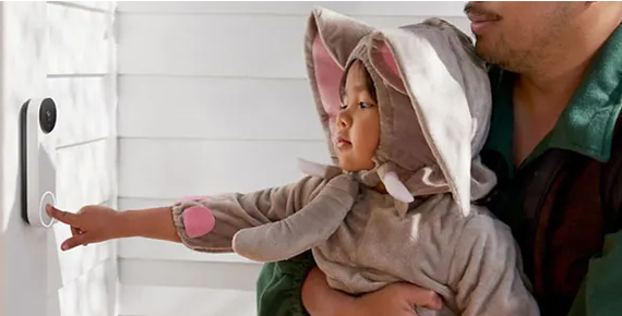 Un enfant tenu dans les bras par son père qui appuie sur le bouton d'une sonnette connectée.