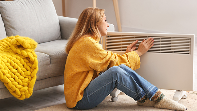 jeune femme se réchauffant auprès d'un radiateur électrique.