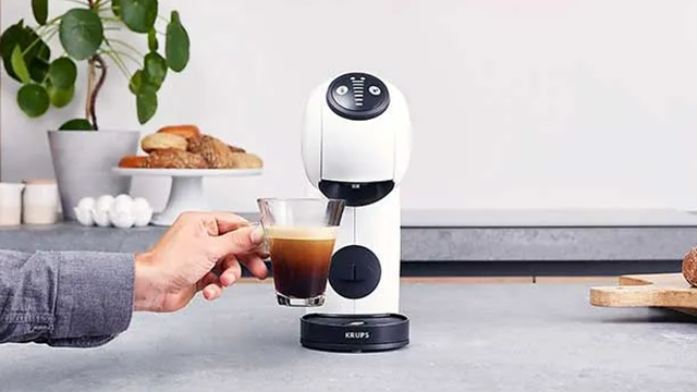 Une personne tient une tasse de café plein devant une machine à café posé sur un plan de travail.