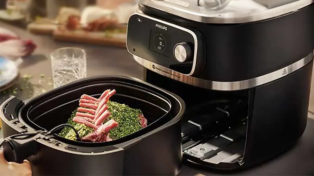 Un airfryer noir. La cuve ouverte est rempli d'aliments prêt à être cuits.
