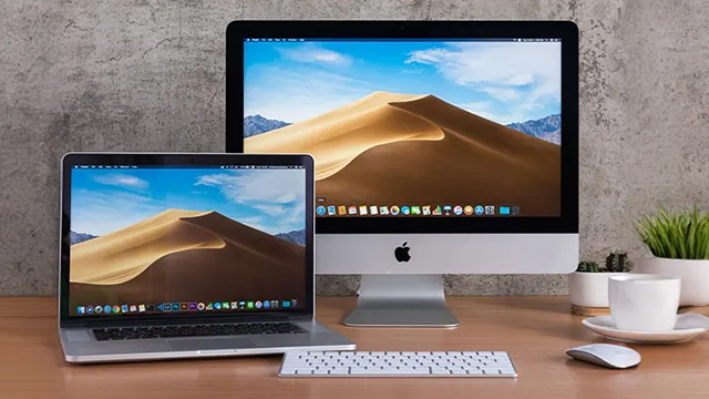 Un MacBook et un iMac posés sur un bureau sur lequel se trouve également un clavier et une souris sans fil.