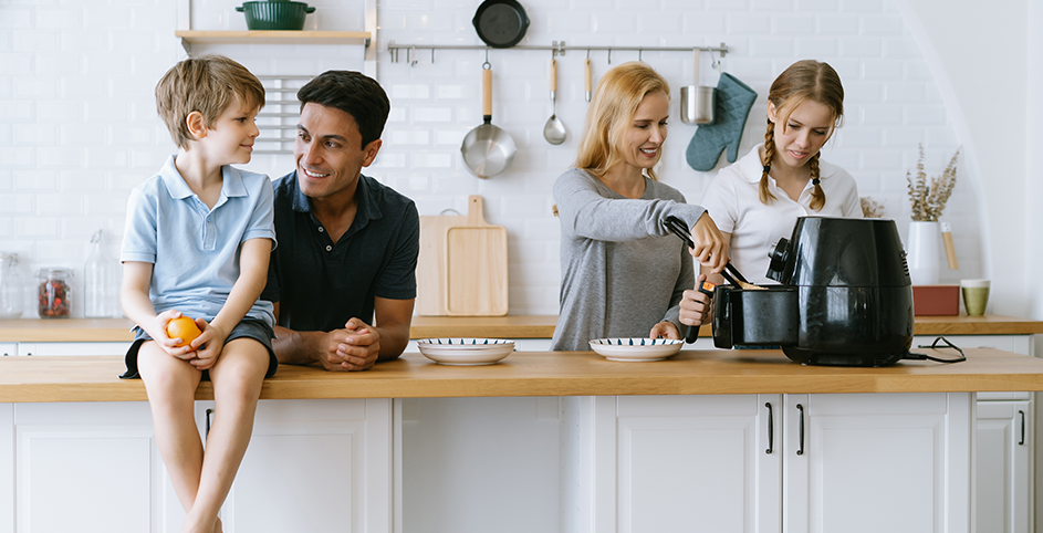 Une famille de 4 personnes dans une cuisine. La mère et la fille cuisinent à l'aide d'un airfryer.