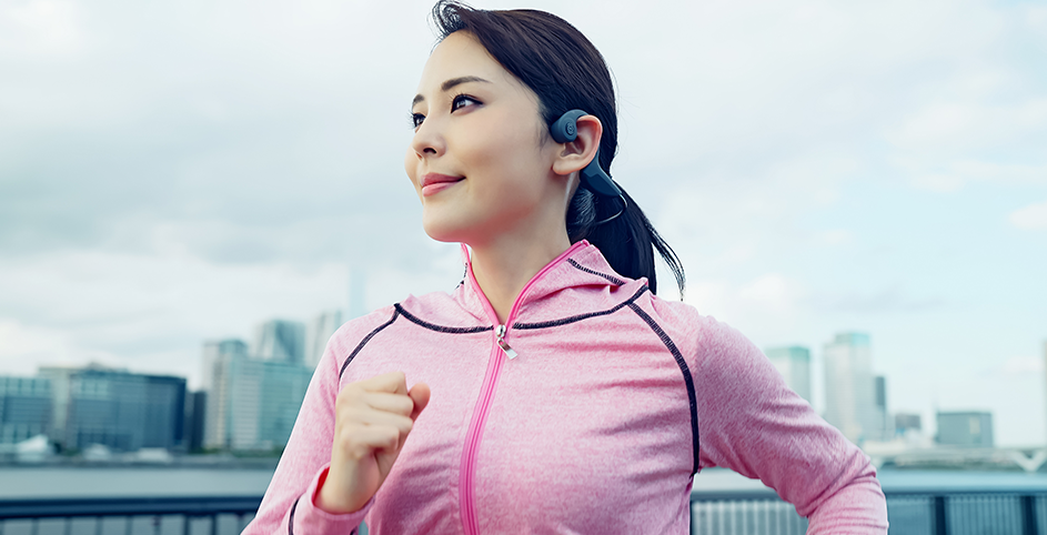 Une femme fait son jogging en ville avec un casque à conduction osseuse dans les oreilles.
