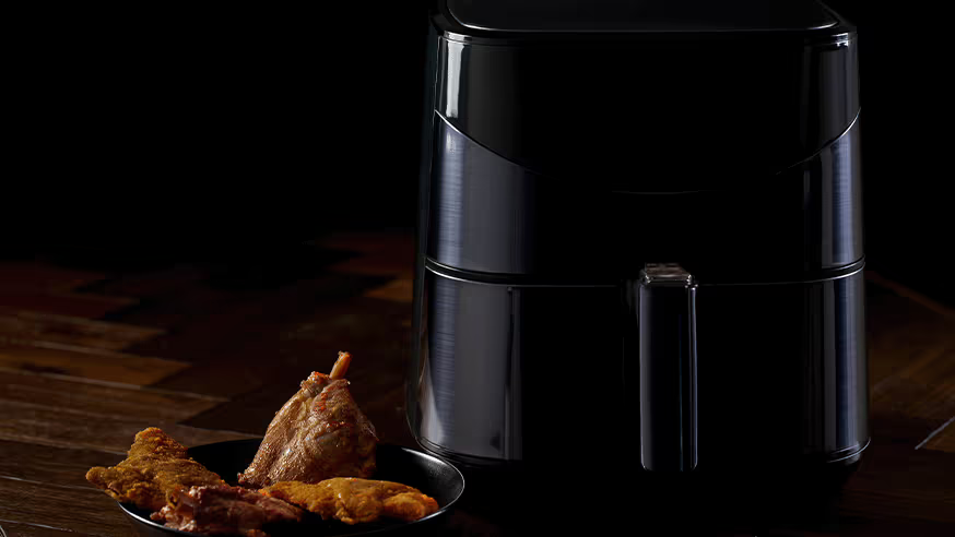 un airfryer posé sur une table avec une assiette à côté dans laquelle se trouve des pilons de poulets.