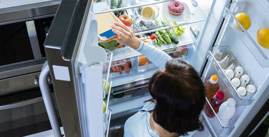 Une femme range des aliments dans un réfrigérateur.