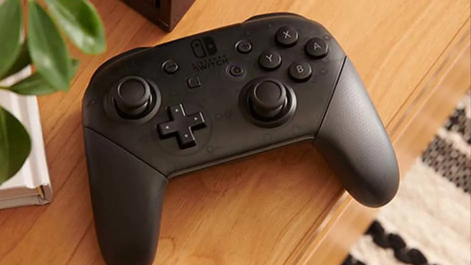 Une manette Nintendo Switch Pro noire posée sur une table en bois, près d’une plante verte.
