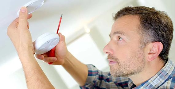 Un homme qui installe un détecteur de fumée au plafond d'un logement.