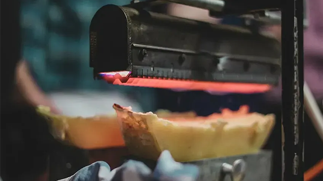 Une demi-meule de fromage fond sous la résistance chaude d'un appareil à raclette.