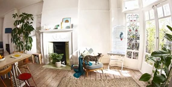 Un salon lumineux avec cheminée, grandes fenêtres, fauteuil et chat, vu par une caméra connectée.