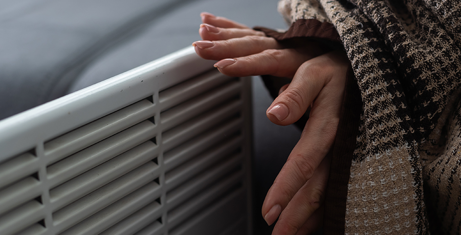 Deux mains à proximité de la grille d'un radiateur électrique pour se réchauffer.