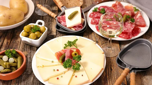 Une table avec des assiettes garnies de fromage, de charcuteries, pommes de terre et cornichons.