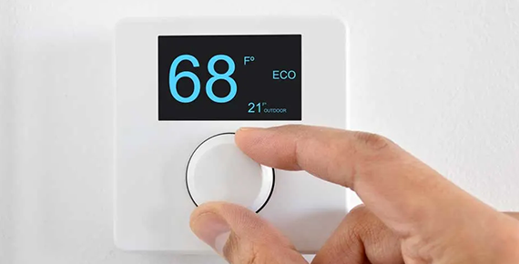 Une main règle le bouton d'un thermostat connecté fixé au mur et affichant 68° F en mode éco.