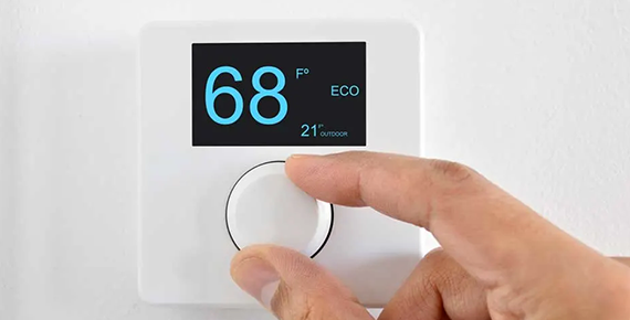 Gros plan sur une une main et un thermostat d'ambiance qui indique une température.