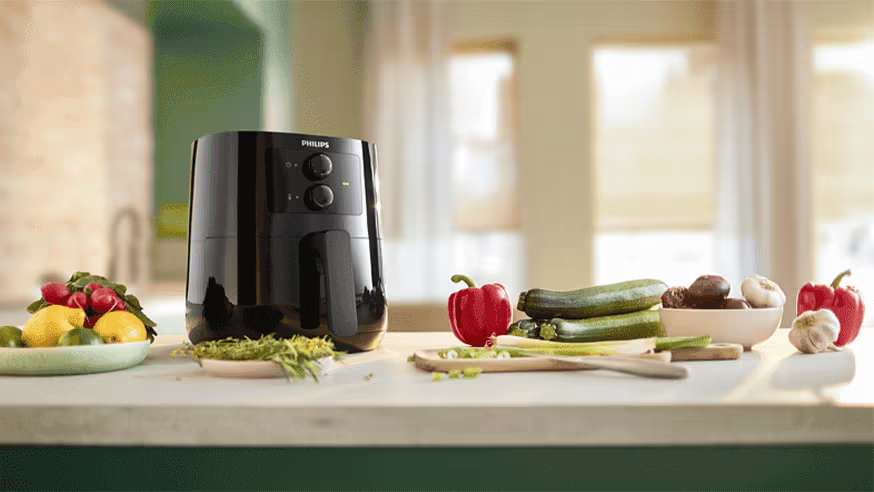 Un airfryer sur une table avec des différents légumes posés dessus.