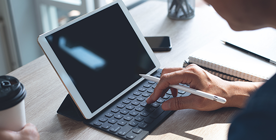 Une personne utilise un iPad avec clavier et Apple Pencil sur un bureau.