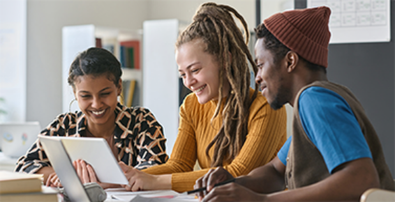 Trois personne souriantes travaillent ensemble sur une tablette et des documents.