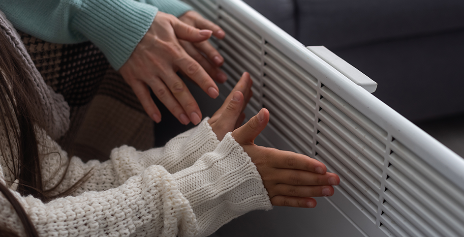 Deux personnes se réchauffent les mains près d'un radiateur électrique blanc.