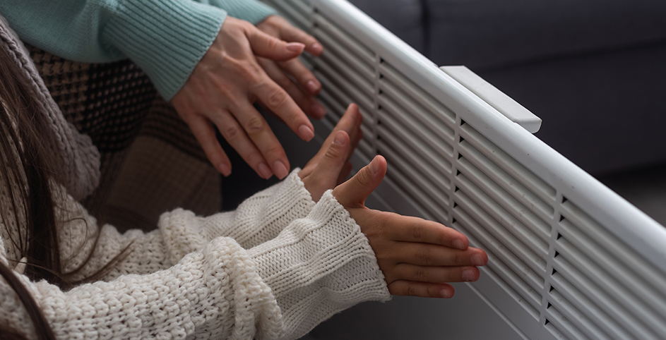 gros plan sur un radiateur électrique et les mains d'un adulte et d'un enfant qui se réchauffent.