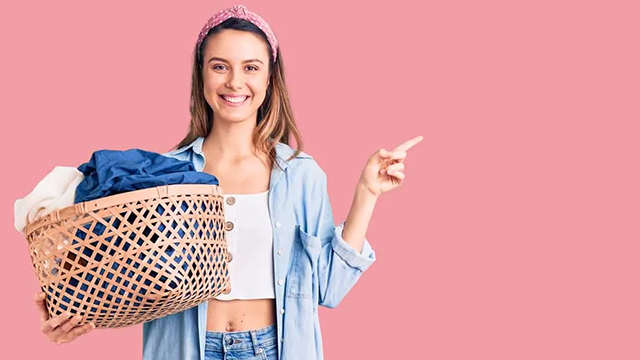 Jeune femme avec un bandana qui tient un panier de linge dans la main sur un fond rose.