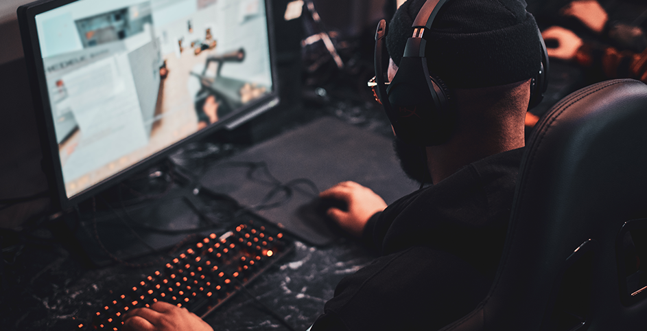 Un joueur portant un casque et un bonnet joue à un jeu de tir sur son ordinateur.