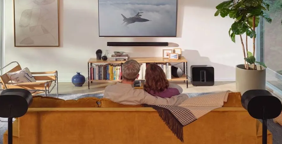 Un couple assis sur un canapé regarde un film d'action sur une TV équipé d'un système audio Sonos.